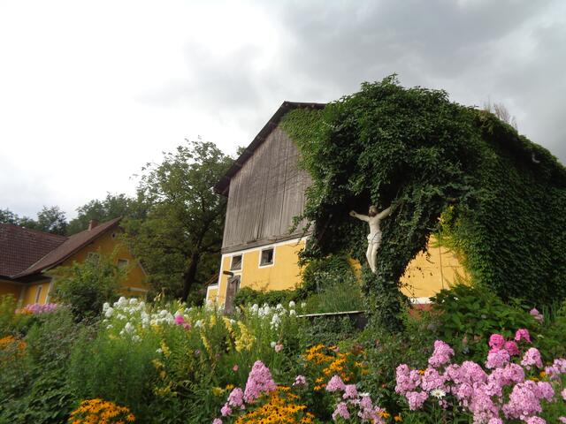 Ein Kruzifix, umgeben von blühender Natur, im Garten von Anna Holzmann erinnert, dass der Tod zum Leben gehört. | Foto: Holzmann