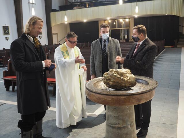 Das Taufbecken mit dem (diskutierten) abgeschlagenen Haupt des Täufers Johannes. – V. l.: Künstler Böhme, Stadtpfarrer Plöbst, Kultur-referent Gsaxner, Bürgermeister Wallner.
