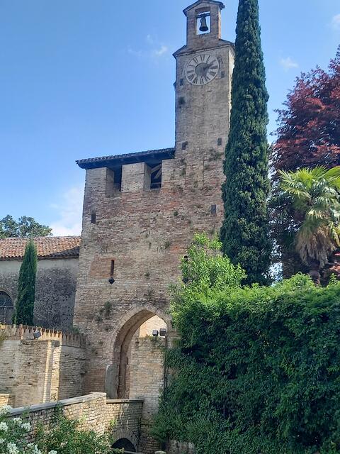 Cordavado. Der Eingang zum Castello di Cordavado und zum Palazzo Piccolomini Freschi. Hinter den Mauern verbirgt sich ein einladender Garten mit hohen Bäumen.