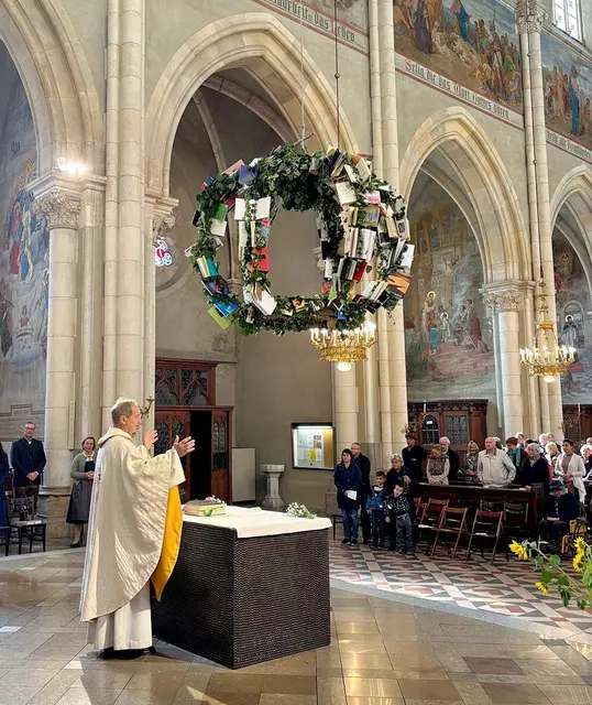 In Graz-Herz Jesu schwebt eine Erntekrone mit alten Büchern über dem Altarraum. Pfarrer Matthias Keil erläutert: Die Bücher sind Zeichen dafür, dass man auch für geistige Gaben dankbar sein kann.  | Foto: Pfarre